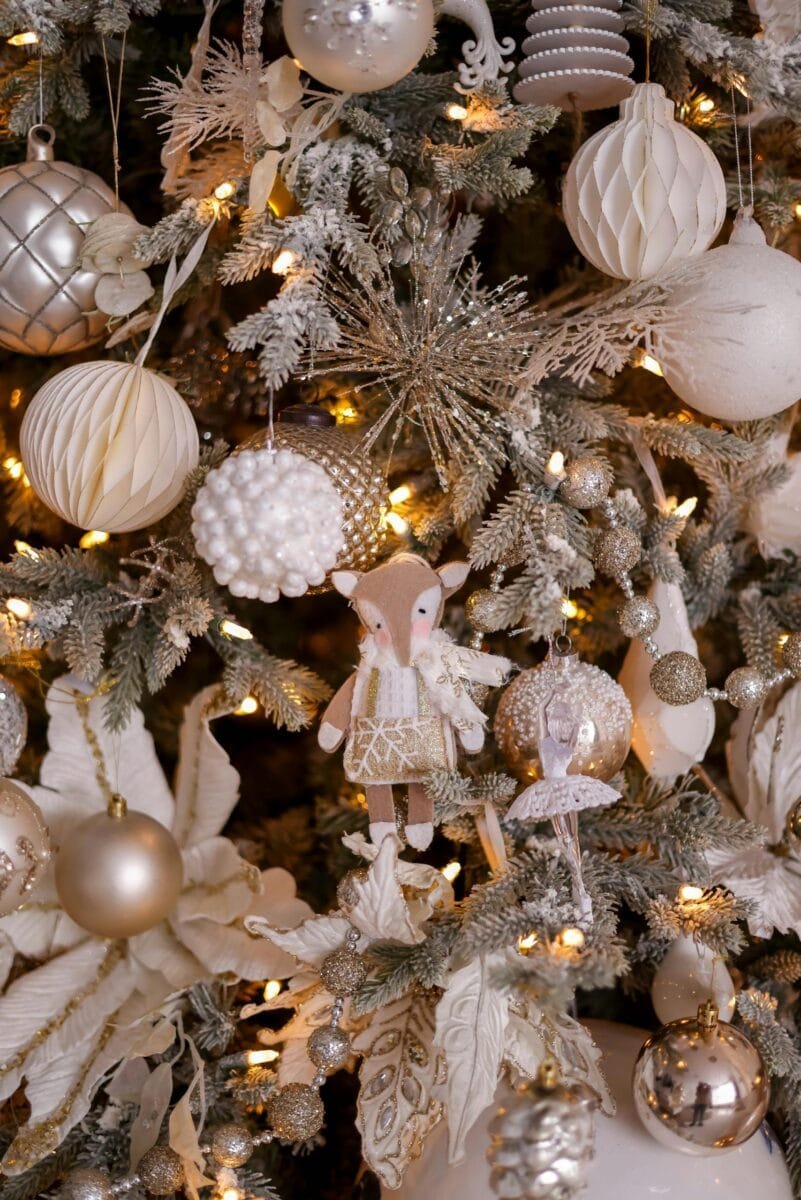 Close-up of a beautifully decorated Christmas tree with gold and white ornaments, sparkling lights, and intricate details.