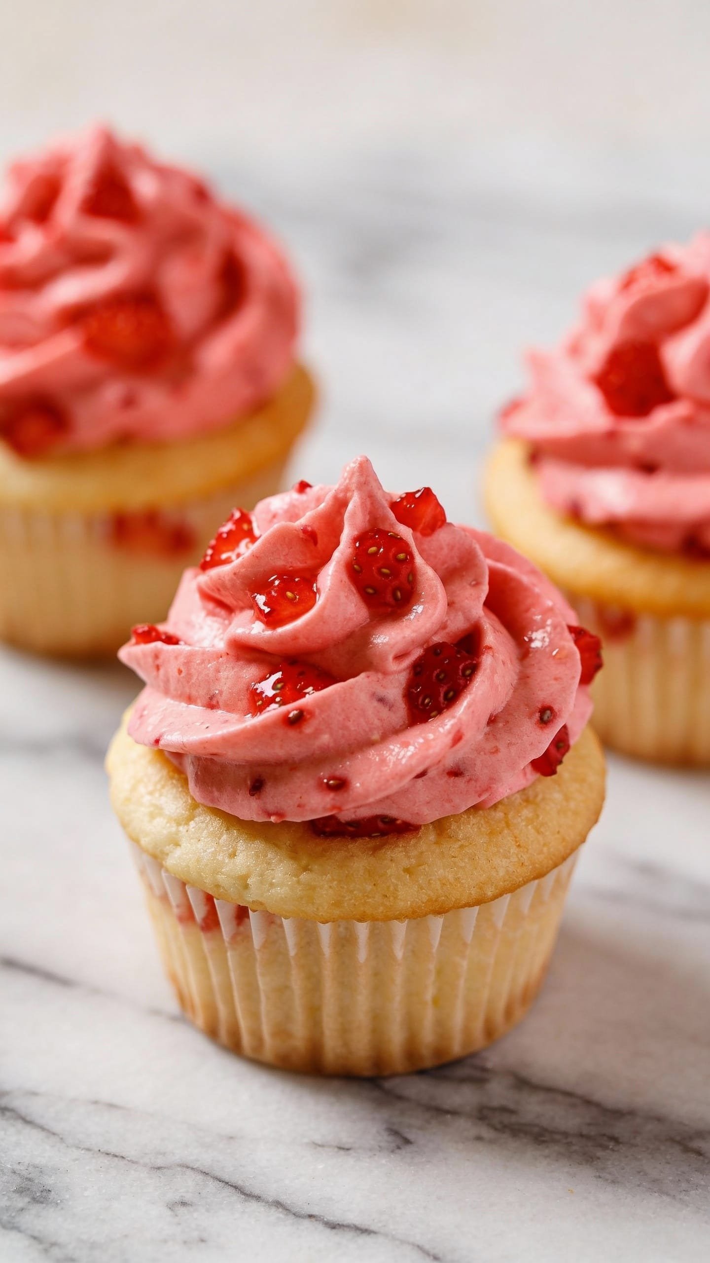 three vanilla cupcakes topped with real strawberry frosting, marble surface