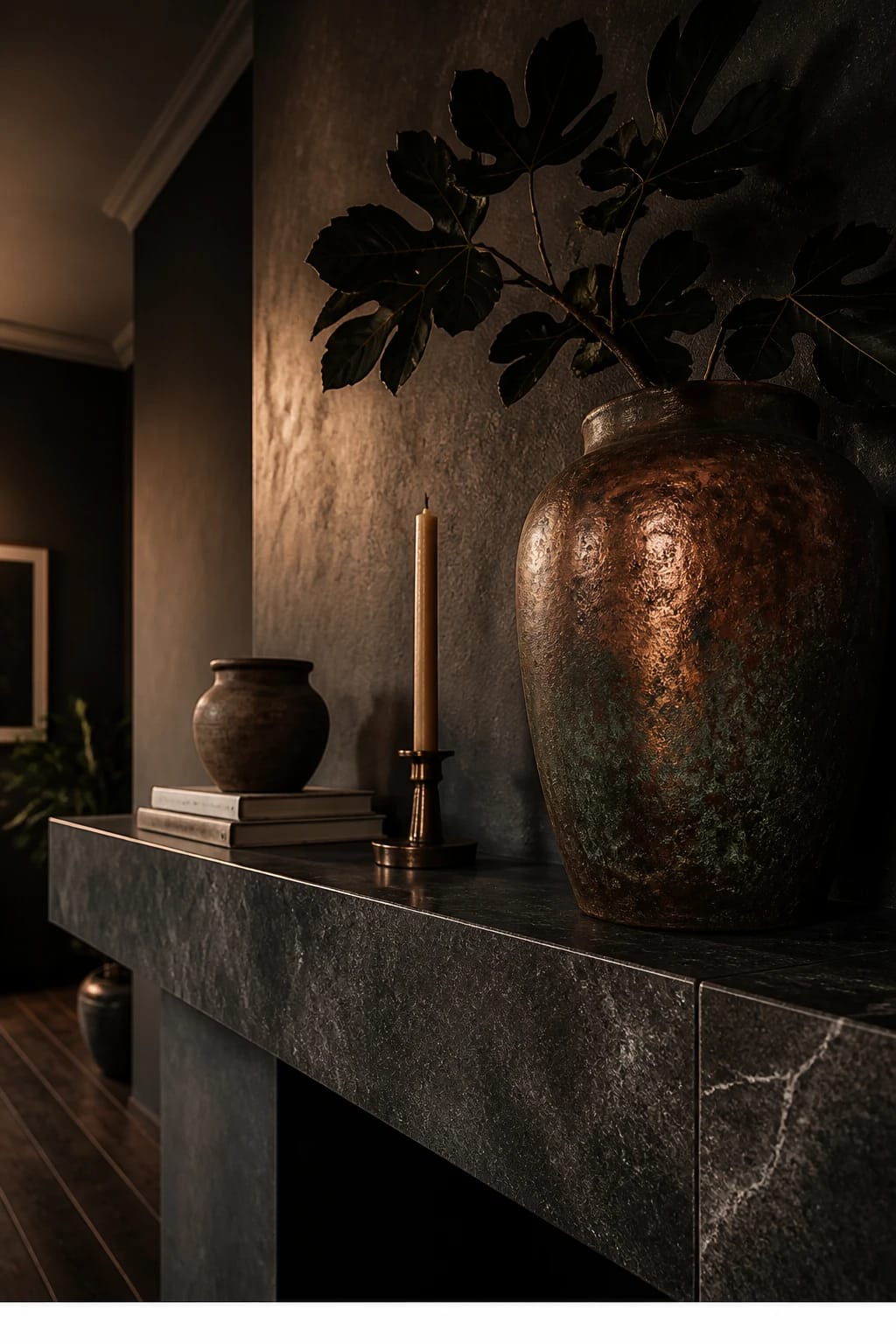 Hero focal point: a collected copper and patina arrangement across the mantel, anchored by a large weathered urn in aged copper dominating the composition. Scene mode. MOODY DRAMATIC LUXE atmosphere with evening edge lighting grazing a charcoal limewash chimney breast and a honed soapstone surround with soft veining. The urn holds a dark fig leaf branch with substantial silhouette. Supporting pieces include a single matte ceramic vessel, a small stack of neutral art books with unreadable spines, and one beeswax taper in a smoked brass holder to maintain one metal finish. Composition is an extreme close-up of texture across the mantel edge, while intersecting walls and a sliver of ceiling are still readable in soft blur. Oak floor stained deep walnut appears at the base. Shadow gaps at all transitions, consistent vertical fluting is absent to avoid conflicts. Vertical 9 by 16, rich tonal depth, film-like grain, no signage or readable labels. Thin white footer strip centered with WWW.HOMESTYLEVIBES.COM